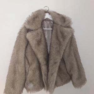 Beige pälsjacka - Säljer en lyxig beige pälsjacka med fluffig textur och bred krage. Jackan har en elegant och varm design, perfekt för kyliga dagar. Den är långärmad och ger en glamorös look. Jackan är ej använd💕