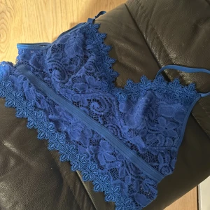 Blå spets linne - Snygg blå spets linne med justerbara axelband. Den har ett vackert blommönster och en bred spetskant nedtill. Perfekt för att lägga till en touch av elegans till din outfit.