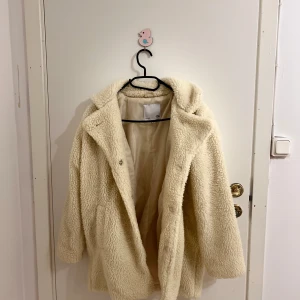Beige teddyjacka från lager157 - Mysig beige teddyjacka från lager 157. Perfekt för våren då de är lite kyligt fortfarande och du vill hålla dig varm och stilren. Jackan har en enkel design med fina knappar på framsidan.