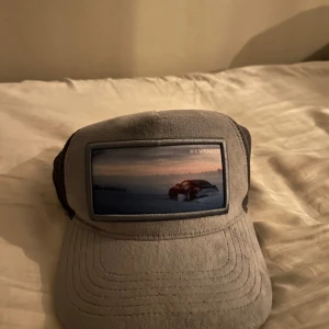 Grå keps revenite - Snygg grå keps från Revenite med ett unikt fototryck på framsidan. Kepsen har en justerbar rem baktill för perfekt passform och är tillverkad i ett lätt och bekvämt material.