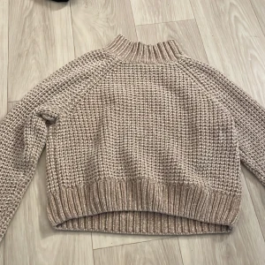 Beige stickad tröja från H&M - Mysig beige stickad tröja från H&M:s Divided-kollektion. Tröjan har en hög krage och långa ärmar, perfekt för kyligare dagar. Den har en ribbad struktur vid ärmslut och nederkant som ger en snygg detalj.