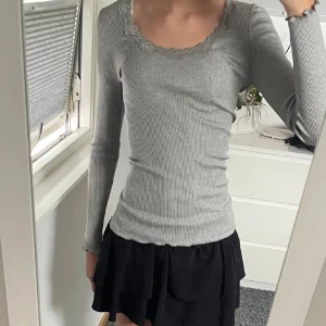 Grå ribbad topp - Säljer en stilren grå ribbad topp med långärmad design och spetsdetaljer vid halsringningen. Perfekt för en avslappnad men ändå elegant look.