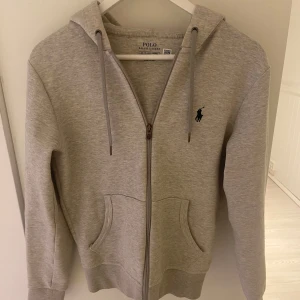 Ralph lauren Hoodie med dragkedja  - Säljer en äkta och stilren grå hoodie från Ralph Lauren med dragkedja. Tröjan är i storlek XS och köpt i USA. Säljer för den är för liten för mig. | Skick 7/10 lite nopprig och så har den en liten fläck på vänster handled, den har också en liten fläck på baksidan av armen men man tänker ej på d | Pris kan diskuteras vid snabb affär 