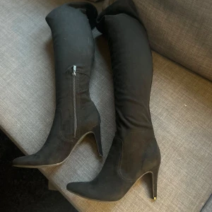 Svarta overknee boots med klack - Snygga svarta overknee boots med hög klack och dragkedja på sidan. Perfekta för en stilren look. Tillverkade i ett material som liknar mocka.