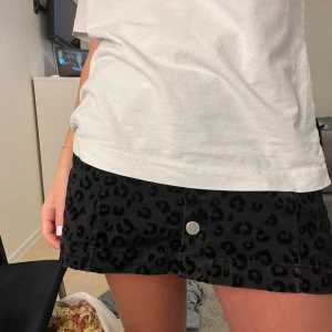 Svart leopardmönstrad kjol med knappar - Trendig svart kortkjol med leopardmönster och knappar framtill. Perfekt för att ge din outfit en djärv touch. Kjolen har en A-linjeform som ger en smickrande passform.