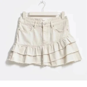 Beige jeanskjol med volanger - Säljer en söt beige jeanskjol med volanger. Kjolen har en kort längd och klassisk jeansdesign med fickor och bälteshällor. Perfekt för en avslappnad och trendig look!