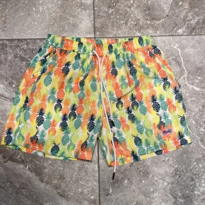 Färgglada badshorts med ananasmönster - Snygga och färgglada badshorts köpt i Miami med ett livligt ananasmönster i grönt, orange, gult och blått. Shortsen har en bekväm elastisk midja med snörning för perfekt passform. Perfekta för sommarens alla badäventyr! 🍍🌞