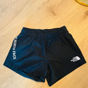 Svarta shorts från The North Face - Snygga svarta shorts från The North Face med elastisk midja och logga på sidan. Perfekta för träning eller en aktiv dag ute. De är tillverkade i ett lätt och bekvämt material som ger bra rörelsefrihet.