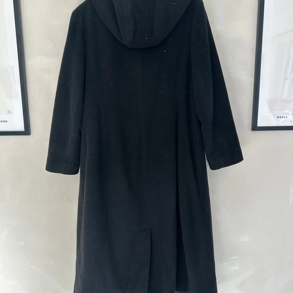 Snygg svart kappa från Index med huva och knäppning framtill. Perfekt för kyligare dagar med sin långa design och stilrena look. Ett måste i garderoben för den som gillar klassisk stil.. Takit.