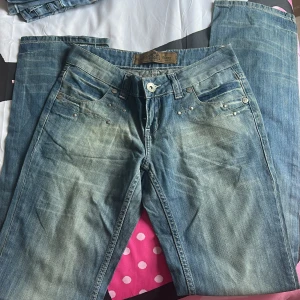 Blå jeans från Rerock - Snygga blå jeans från Rerock med en klassisk femficksdesign och subtila slitningar för en trendig look. De har en knappgylf och nitar vid fickorna som ger extra stil. Perfekta för en avslappnad vardagsstil.