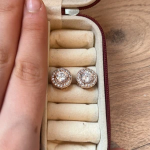 Glittriga örhängen med stenar - Säljer ett par eleganta glittriga örhängen med stora centrala stenar omgivna av mindre gnistrande stenar. Perfekta för att ge en touch av glamour till din look. Kommer i en praktisk förvaringsask.