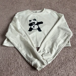 Vit croppad tröja med panda-tryck - Säljer en vit croppad tröja med ett coolt panda-tryck på framsidan. Tröjan har långa ärmar och en avslappnad passform. Perfekt för en avslappnad stil!
