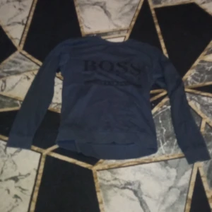 Mörkblå tröja från Boss - Säljer en mörkblå tröja från Boss i slim fit. Tröjan har långa ärmar och ett diskret tryck på framsidan. Perfekt för en stilren look.