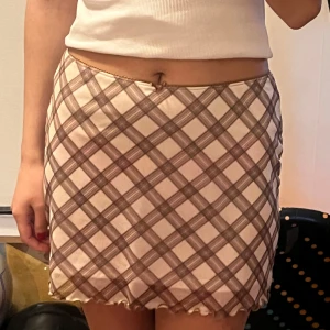 Kjol rutig - Snygg kortkjol med rutigt mönster i beige och brun. Kjolen har en enkel design med en lätt volangkant nedtill. Perfekt för en trendig look och aldrig använts. Pris går att diskutera ✨