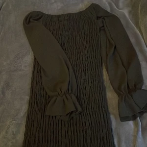 Svart offshoulder klänning - Snygg svart offshoulder klänning med långa ärmar och volangdetaljer vid ärmsluten. Perfekt för en stilren look.