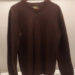 Brun tröja från Chevalier - Säljer en brun tröja från Chevalier i storlek XL. Tröjan har en v-ringad design och långa ärmar. Perfekt för kyligare dagar med sin varma och bekväma känsla. Märkeslogga på ärmen ger en extra touch.