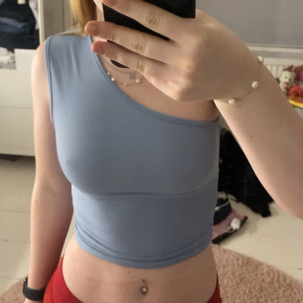 Säljer en stilren ljusblå oneshoulder topp. Den är ribbad och croppad, perfekt för en trendig look. Toppen har en tight passform som framhäver figuren. Kommer inte ihåg var den är köpt och lappen är ej kvar så vet ej storleken.. Yläosat.