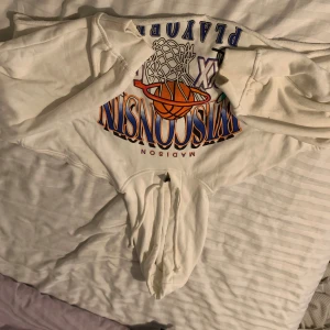 Vit crop topp hoodie från H&M  - Säljer en vit hoodie från H&M med ett färgglatt tryck på framsidan. Hoodien har långa ärmar och en klassisk känguruficka framtill. Perfekt för en avslappnad stil.