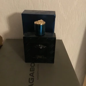 Versace Eros Eau de Toilette cirka 85ml - Säljer en flaska Versace Eros Eau de Toilette, 100 ml. Flaskan är mörkblå med ett elegant mönster och har en guldig kork. Perfekt för den som vill ha en fräsch och maskulin doft. Flaskan är nästan full och kommer i originalförpackning. Passa på att köpa denna lyxiga parfym till ett bra pris! Cirka 85 ml kvar
