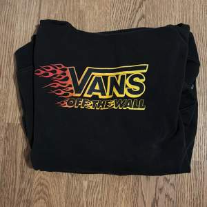 Säljer en svart hoodie från Vans med coolt tryck i gult och rött. Den har en stor ficka fram och texten 'Off The Wall' på ärmen. Perfekt för en avslappnad stil!