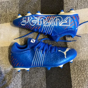 Puma fotbollsskor  - Säljer ett par snygga blå fotbollsskor från Puma i mycket bra skick. Skorna har en cool design med vita och orange detaljer samt snörning för perfekt passform. Perfekta för fotbollsträning eller match!