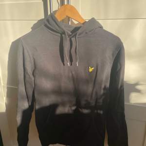 Säljer en snygg svart hoodie från Lyle & Scott i mycket bra skick. Den har en gul broderad logga på bröstet och en praktisk magficka. Perfekt för höst och vinter, och passar både till vardags och chillkvällar. Storleken är normal och materialet är mjukt och bekvämt.