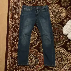 Säljer ett par klassiska Levi's 515 jeans i blå denim. De har en snygg straight passform och är i mycket bra skick. Perfekta för både vardag och fest! Dragkedja och knapp framtill för enkel stängning. Passar bra till alla säsonger och stilar.