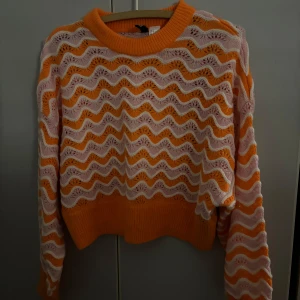 Orange och vit stickad tröja från h&m - Säljer en superfin orange och vit stickad tröja från Divided h&m. Den har ett vågigt mönster och är croppad med långa ärmar. Perfekt för höst och vår! 🧡