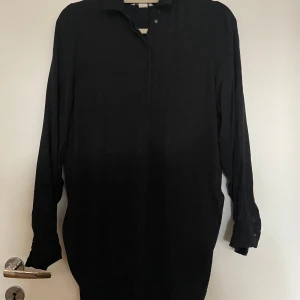 Svart långärmad skjorta från H&M - Snygg svart långärmad skjorta från H&M i storlek 34. Perfekt för både vardag och fest. Skjortan har en klassisk krage och knappar framtill. Den är i mycket bra skick och passar till alla säsonger. Enkelt att matcha med olika outfits! Lång i modellen , mer åt runika-längd.