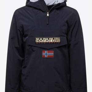 Säljer en svart vindjacka från Napapijri med en stor ficka framtill och norsk flagga som detalj. Jackan har en huva och dragkedja vid halsen. Perfekt för blåsiga dagar och har en stilren look. Passar både till vardags och utomhusaktiviteter. I mycket bra skick!