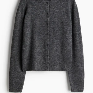 Mörkgrå kofta - Säljer en stilren och mysig mörkgrå kofta med knappar framtill. Perfekt för kyliga dagar och passar till det mesta i garderoben. Koftan har långa ärmar och en klassisk design som aldrig går ur tiden. Ett måste för höst- och vintergarderoben!