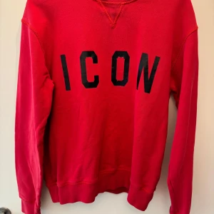 Dsquared2 med 'ICON' tryck (M) - Säljer en röd dsquared2 sweatshirt med svart 'ICON' tryck på framsidan. Tröjan har långa ärmar och är perfekt för en avslappnad stil. Den är i bra skick och passar perfekt för höst och vår. Perfekt för dig som vill sticka ut lite extra! OBS! Tröjan är äkta. Finns ett minimalt lagat hål på baksidan som inte syns.