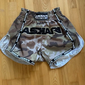 Askari camouflage shorts - Säljer ett par camo-shorts från Askari. Perfekta för kampsport. De har en loose passform och är gjorda i slitstarkt material. Elastisk midja. Dom är i nyskick. Storleken funkar för iprincip alla över 180cm eller om man är lite större så funkar de oavsett. 