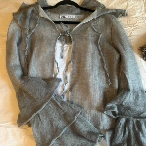 Grå stickad kofta från Zara - Säljer en superfin grå stickad kofta från Zara. Den har volangdetaljer och knytband framtill som ger en söt touch. Perfekt för höst och vår när du vill ha något mysigt men ändå snyggt!! Så söööt, använd en gång!❤️liten i storlek m är perfekt