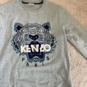 Säljer en snygg ljusblå sweatshirt från Kenzo med deras ikoniska tigerbroderi i blått och vitt på framsidan. Tröjan är i mycket bra skick och perfekt för både vardag och fest. Den har långa ärmar och en bekväm passform. Perfekt för att ge din outfit en cool touch! 🐯