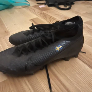 Svarta fotbollsskor - Säljer ett par svarta fotbollsskor i bra skick. De har snörning och en liten svensk flagga på sidan Skorna har en stilren design och är bekväma att spela i. Det går att pilla bror Sverige märket om man skulle vilja de