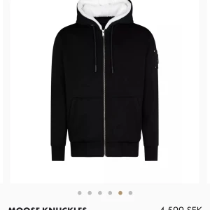 Svart hoodie från Moose Knuckles - Säljer en snygg svart hoodie från Moose Knuckles med vit fleecefoder i luvan. Den har dragkedja framtill och långa ärmar. Perfekt för höst och vinter, håller dig varm och stilren. Passar både till vardags och chillkvällar. I väldigt bra skick, använd Max 5 gånger då den inte passar mig. Kostar som ny 4.600kr.