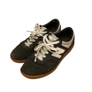 Svarta sneakers från New Balance - Säljer ett par svarta New Balance sneakers i bra skick. De har en snygg kombination av mocka och syntetmaterial med vita detaljer och snörning. Perfekta för både vardag och träning. Sulan är brun och ger en cool kontrast. Passar perfekt till höst, vinter och vår! Har dock ett litet hål som knappt syns eller känns i bakre delen av sulan. 
