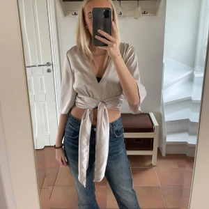 Beige omlottopp med knytband - Säljer en superfin beige omlottopp med knytband i midjan. Perfekt för både vardag och fest! Passar bra till både jeans och kjol. 
