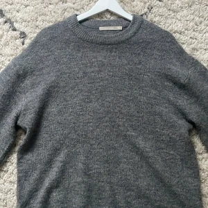 Grå stickad tröja - Mysig grå stickad tröja som i överlag är i mycket bra skick, lite nopprig här och där. Perfekt för kyliga höst- och vinterdagar. Tröjan har långa ärmar och ribbstickade muddar vid ärmslut och nederkant. Enkel och stilren design som passar till det mesta. Ett måste i garderoben för den som älskar komfort och stil! 