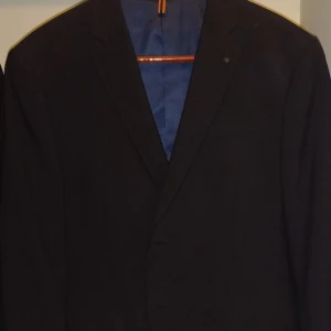 Svart kavaj från Glenn Strömberg - Snygg svart kavaj från Glenn Strömberg i storlek 52. Perfekt för både fest och formella tillfällen. Kavajen har en klassisk design med knappar framtill och en stilren passform. Ett måste i garderoben för en stilren look!