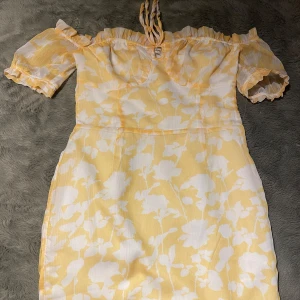Gul och vit blommig klänning - Söt gul och vit klänning med blommigt mönster. Offshoulder-stil med korta ärmar och en bekväm passform. Perfekt för sommarens fester eller en dag på stan. Klänningen har en lätt och luftig känsla.