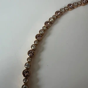 Roséguld pläterat armband med stenar - Säljer ett elegant roséguldarmband med glittriga stenar i rosa o kristall. Armbandet har en säker låsning och är perfekt för att ge en touch av glamour till vilken outfit som helst. Passar både till vardag och fest!