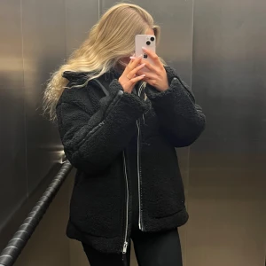 Svart teddyjacka - Mysig svart teddyjacka perfekt för kyliga dagar. Den har en dragkedja framtill och är långärmad. Jackan är i bra skick och passar perfekt för höst och vinter. Den är både stilren och bekväm, vilket gör den till ett måste i garderoben!