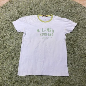 Vit t-shirt från Zara Jeans - Säljer en vit t-shirt från Zara Jeans med texten 'Malambo Surfing' i grönt på framsidan. T-shirten har en gul och grön ribbad krage och är kortärmad. Perfekt för en avslappnad sommarlook eller en dag på stranden. 🏄‍♂️