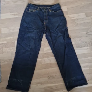 Blå jeans med broderade bakfickor - Säljer ett par coola blå jeans med unika broderade mönster på bakfickorna i storlek 36. De har en loose passform och är perfekta för en avslappnad stil. Jeansen har en dragkedja och knappar framtill.  De har varit uppvikta vid användning och han har varit cirka 170 lång. 