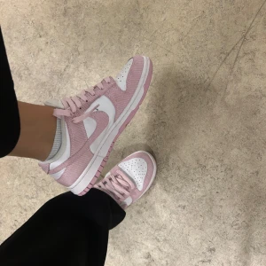 Nike Dunk  - Säljer ett par snygga Nike Dunk sneakers i rosa och vitt. De är i mycket bra skick och har en klassisk design med snörning. Perfekta för vår och sommar. Sköna att gå i och riktigt trendiga just nu!