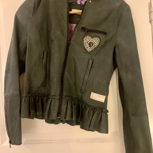 Grå skinnjacka från Odd Molly stl 1 - Säljer en supercool grå skinnjacka från Odd Molly. Mjukt fint skinn. Den har ett hjärta av metall på bröstet och snygga blommönster i pärlor på ryggen. Jackan har en dragkedja fram och volangdetaljer längst ner. Insidan är fodrad med ett vackert tyg. Passar både till vardags och fest, den här jackan är unik. Skicket är väldigt bra, säljer pga den är för liten för mig tyvärr. 