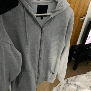 Grå hoodie med dragkedja - Säljer en stilren grå hoodie i mycket bra skick. Den har en praktisk dragkedja framtill och en skön huva. Perfekt för både höst och vår, och funkar lika bra till vardags som till träning. Storlek L för herrar. Passa på att fynda denna mångsidiga tröja!