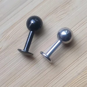 Piercingsmycken stud/labret silverfärgad/svart - Vet inte exakt, men mäter tjockleken till 2mm eller lite mindre än 2mm. Längd 5-6mm, kulor diameter 5. Osäker på material, men tror det är kirurgiskt stål. Den svarta kulans färg är lite skavd.